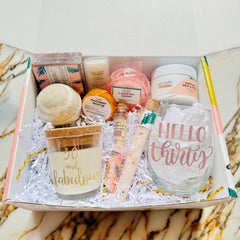 Gift box with 30 and fabulous candle, Hello Thirty rose gold lettered wine glass, lip balm, bath salts, bath bomb, shower bomb, matches, soap, mini lotion bar, loofah soap and lotion. Box is on a white and bronze marbled countertop.